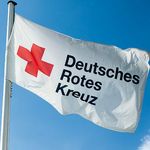 Im Wind weht eine weiße Flagge. Sie zeigt ein rotes Kreuz. Daneben steht in schwarzen Buchstaben: Deutsches Rotes Kreuz.