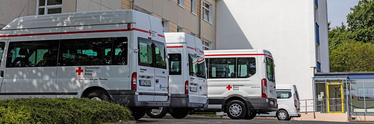 Mehrere Transporter mit DRK-Schriftzug stehen vor einem Gebäude.